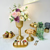 Elegant gold cylinder flower vases with floral arrangements and small pastries on a white table.