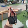 A hand holds a black mini house handbag with a wrist strap against a blurred outdoor background.