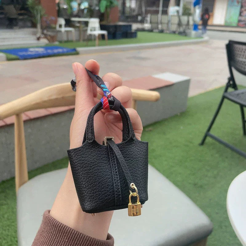 A hand holds a black mini house handbag with a wrist strap against a blurred outdoor background.