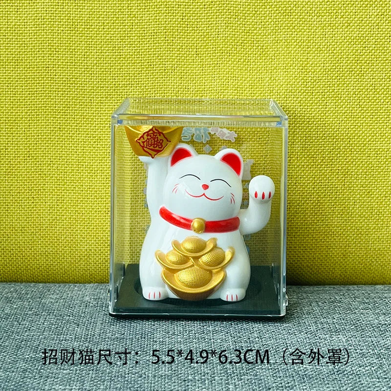 A white ceramic figurine of a waving lucky cat with gold accents displayed in a clear glass box.