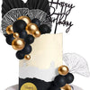 A white cake decorated with black and gold spherical toppers and a black fan-shaped topper for a birthday celebration.