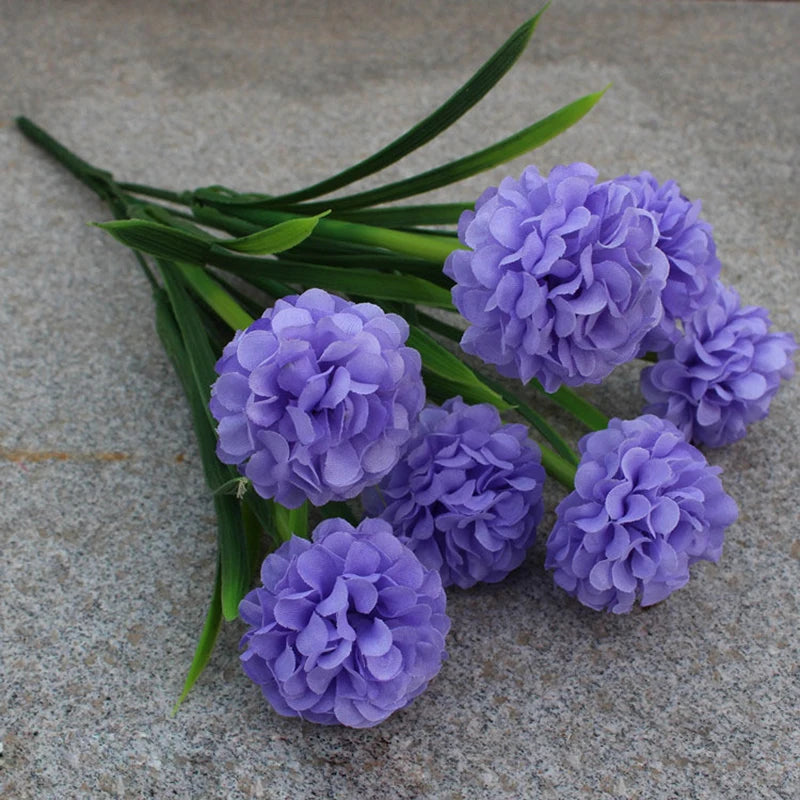Un bouquet de fleurs d'hydrangea artificielles violettes avec de longues tiges vertes sur une surface grise.
