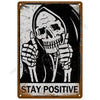 A vintage tin sign featuring a skull with raised fingers and the text STAY POSITIVE on a distressed background.