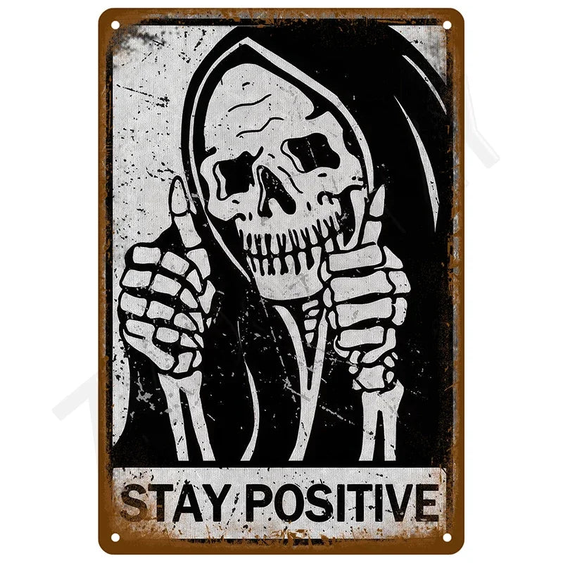 A vintage tin sign featuring a skull with raised fingers and the text STAY POSITIVE on a distressed background.