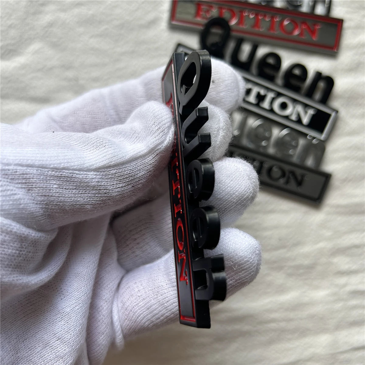 Eine Hand in weißer Handschuh hält ein Set schwarzer und roter Queen Edition Emblem-Autokleber.