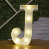 A glowing warm white LED alphabet letter light shaped like the letter J resting on a wooden surface.