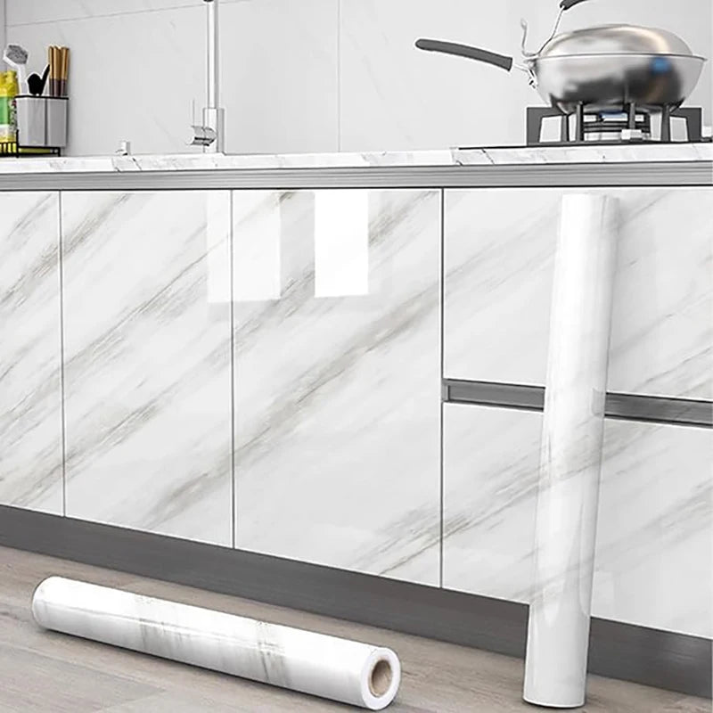 A roll of white marble self-adhesive wallpaper displayed next to kitchen cabinets and a stainless steel pot.