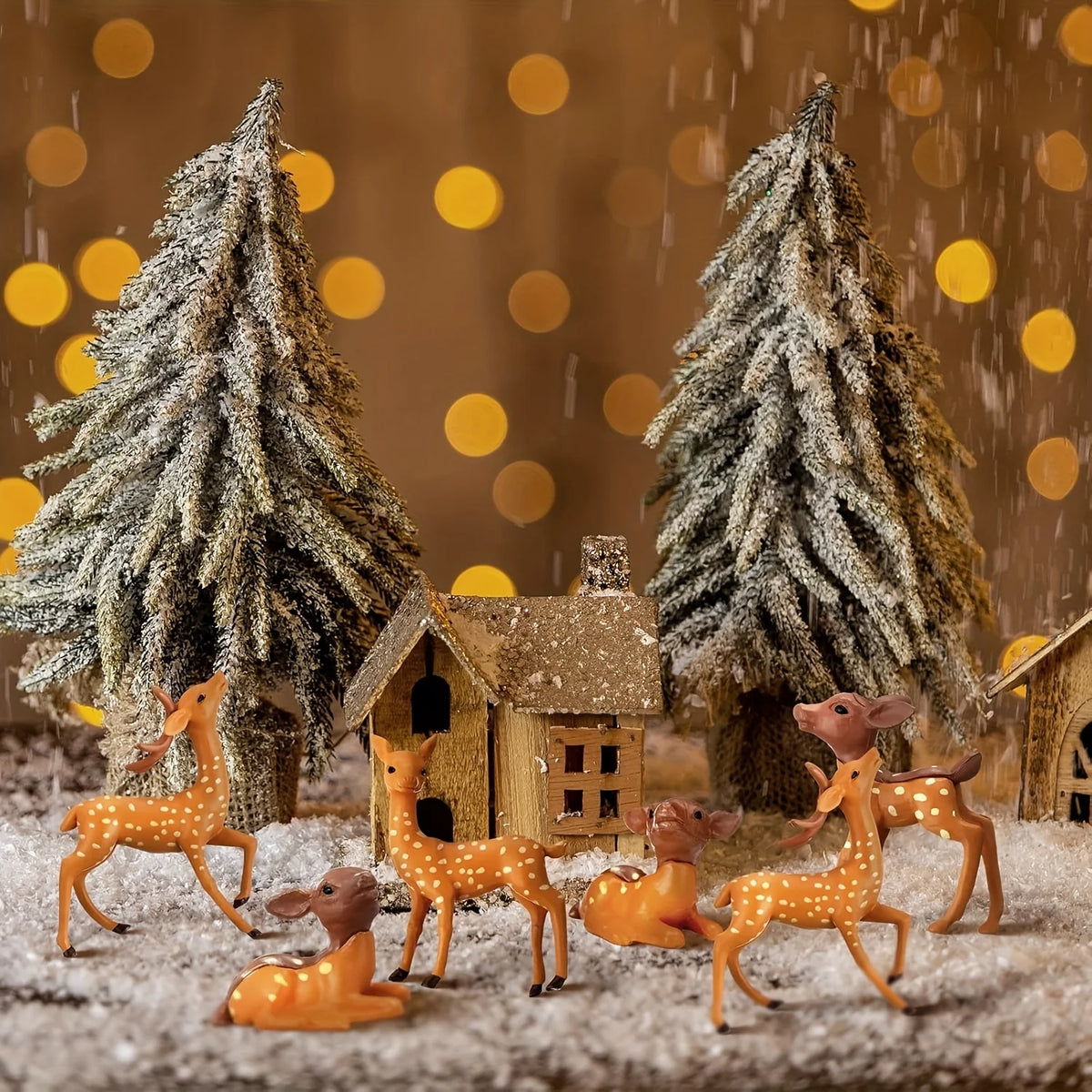 A set of mini deer figurines in various colors standing in a snowy outdoor scene with evergreen trees and a small wooden hous