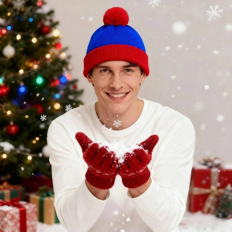 A smiling man wearing a blue and red knitted beanie and red gloves, holding white powder in a snowy festive setting.