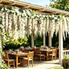 A wooden outdoor dining area decorated with white silk wisteria hanging vine garlands and greenery.