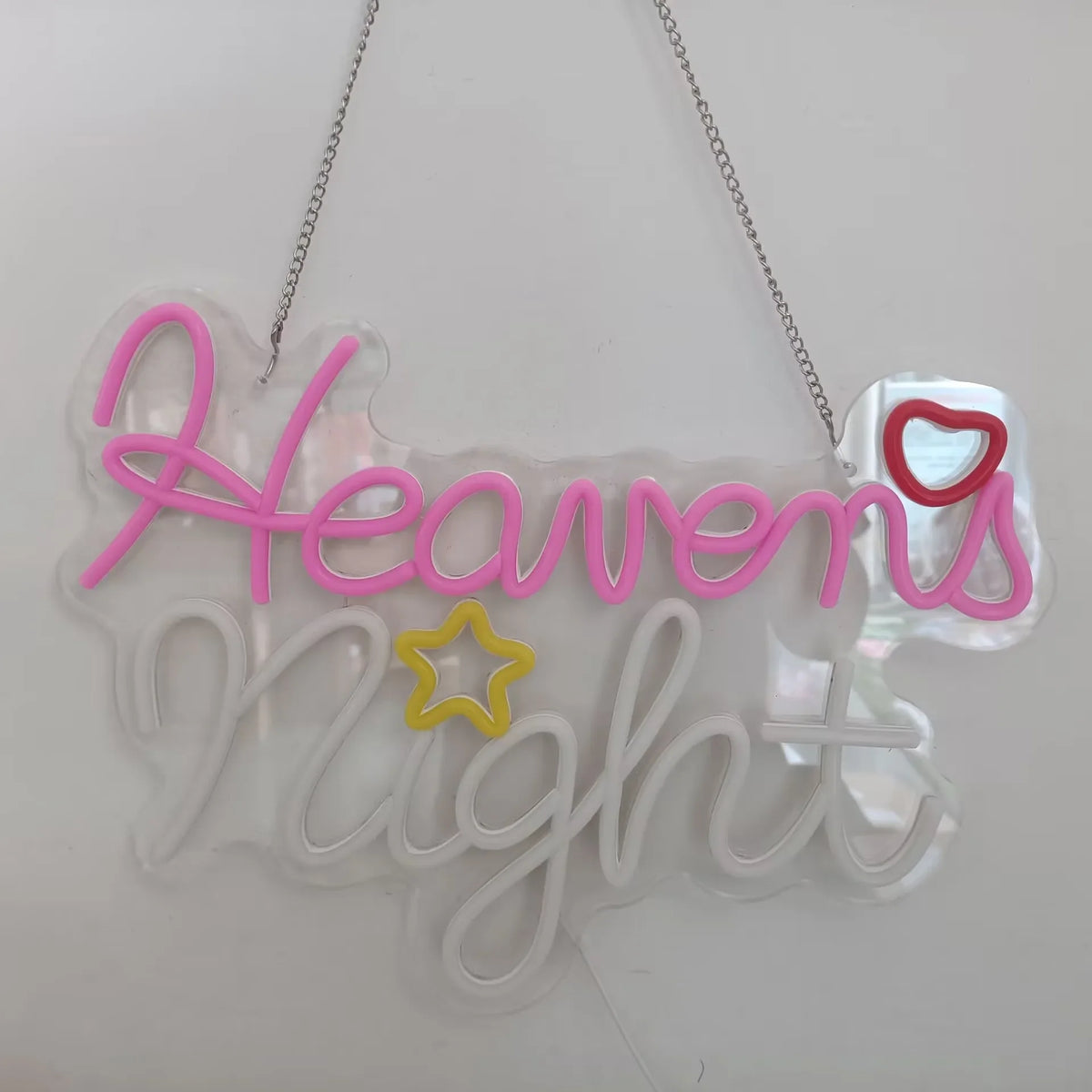 A clear acrylic neon sign shaped like the word Heaven's Night with pink and yellow lettering.