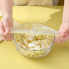 Hands holding a clear cling film sheet above a glass bowl filled with sliced cabbage for food storage