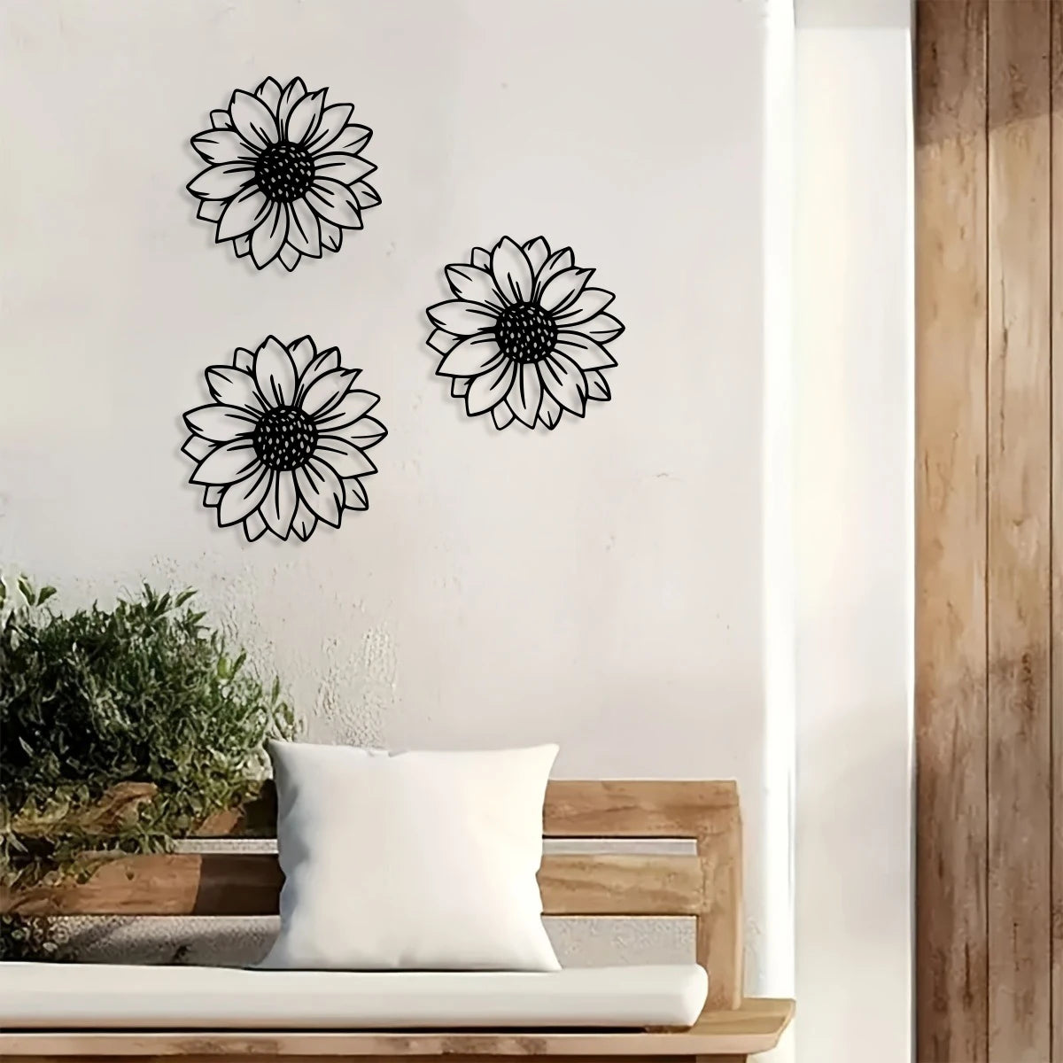 A set of three black metal sunflower wall decorations displayed on a white wall next to a wooden bench.