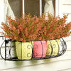 Three potted artificial fall flowers in yellow and pink ceramic pots displayed on a black wire rack.
