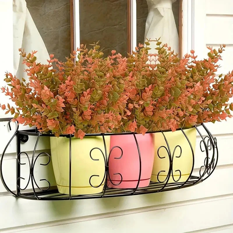 Three potted artificial fall flowers in yellow and pink ceramic pots displayed on a black wire rack.