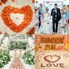 Forme de cœur faite de pétales de roses de soie orange, décorée pour un mariage ou un événement.