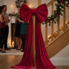 A large, deep red velvet bow with long draping tails is displayed on a wooden staircase railing.