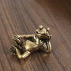 Antique brass sleeping frog figurine with a whimsical pose resting on a dark wooden surface.