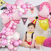 A pink and white balloon wreath archway set decorated with balloons and a baby wearing a party hat.