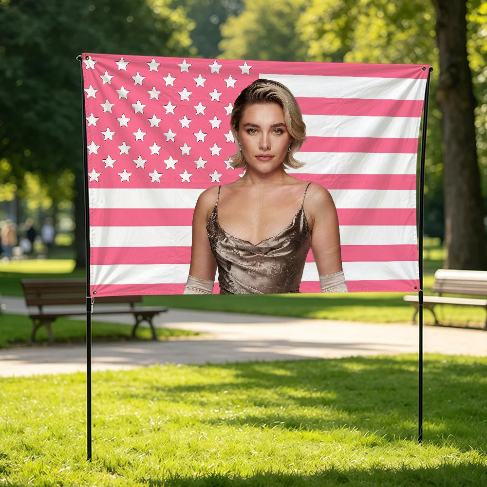 A woman wearing a sheer top stands in front of a pink and white American flag banner in a park setting.