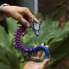 A hand holds a color-changing flexible dragon figurine with vibrant purple and green scales.
