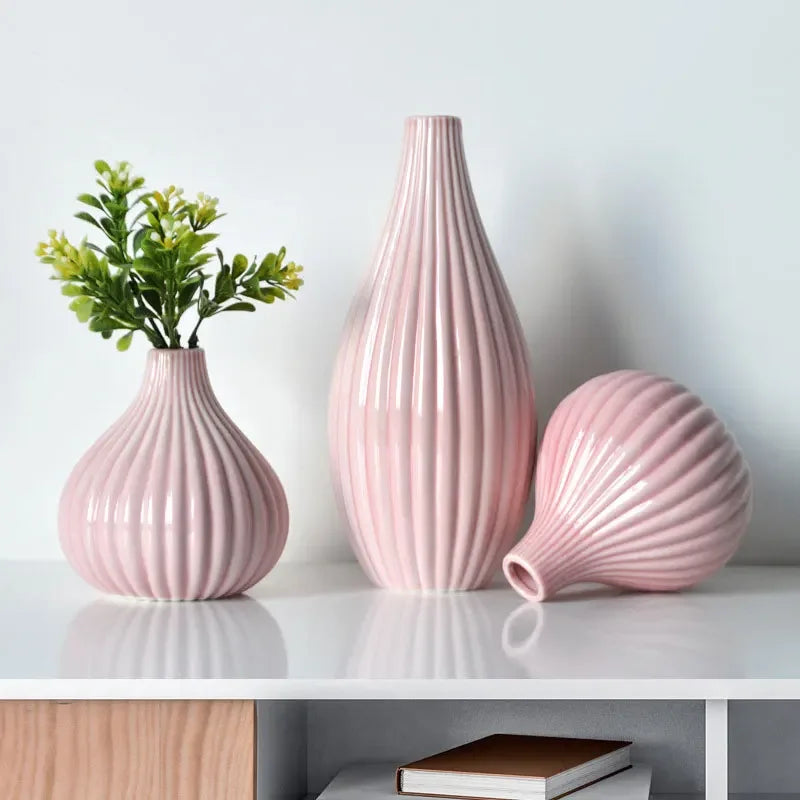 A pink ceramic flower vase with vertical ridges and a matching spherical vase on a white shelf.
