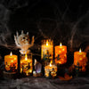 A collection of glowing pillar candles and a skull decoration set against a dark, smoky background for Halloween decor.