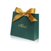 A dark green paperboard thank you gift bag tied with a gold ribbon, featuring the word Merci printed on it.