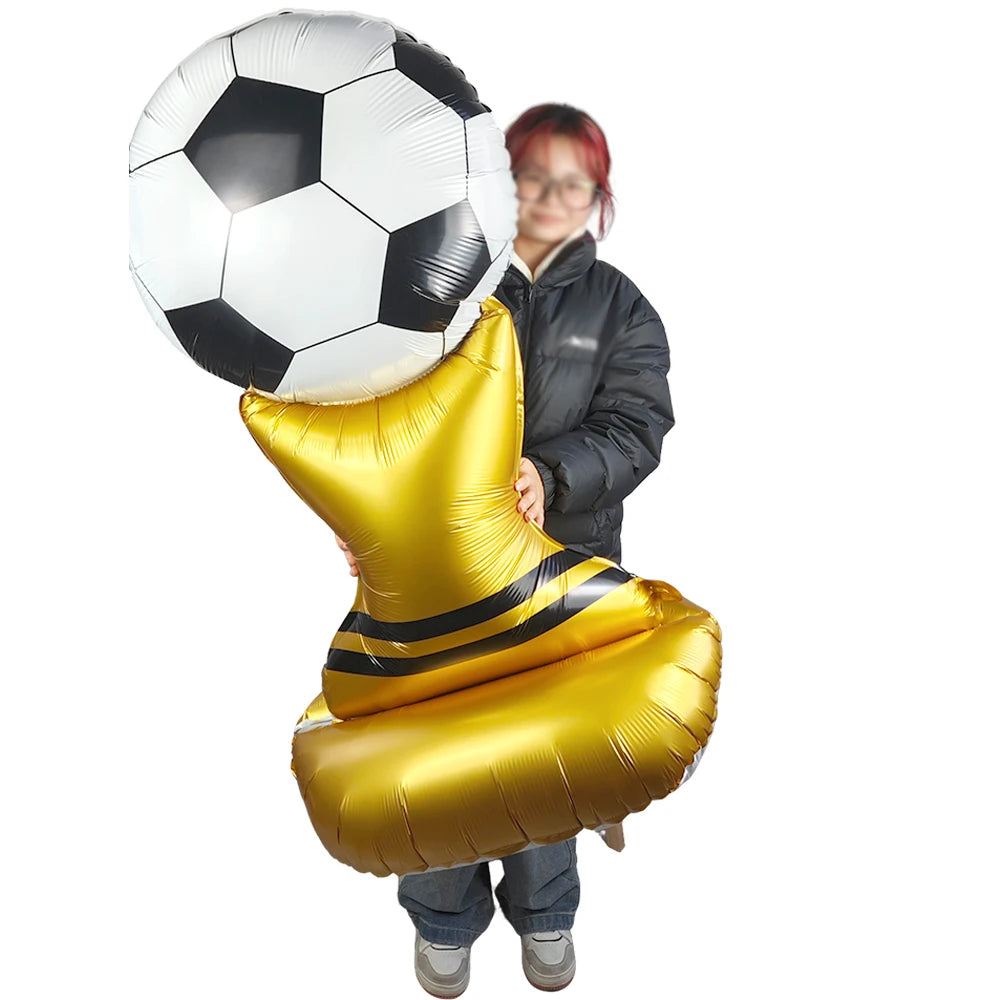 A person is holding a large inflatable soccer ball and a gold balloon shaped like a football.