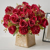 A vibrant bouquet of deep red and burgundy artificial silk flowers, including roses and carnations, arranged in a textured go