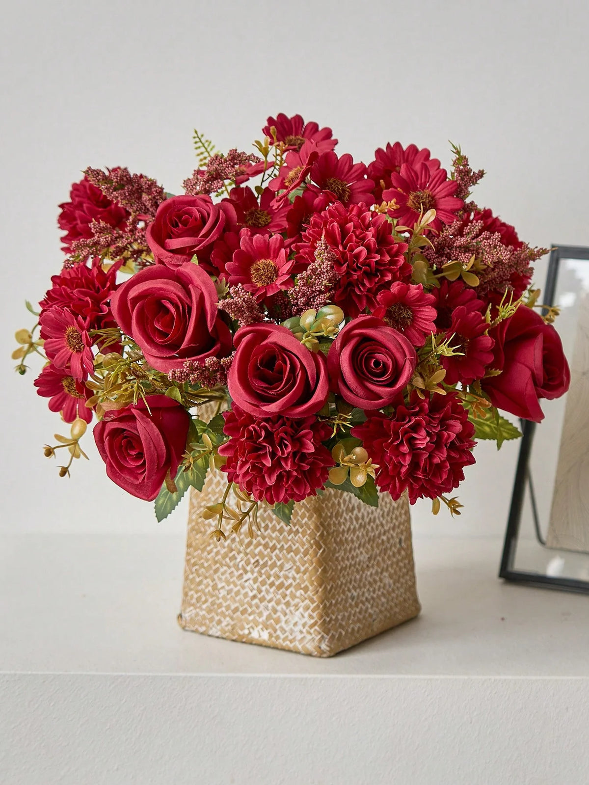 A vibrant bouquet of deep red and burgundy artificial silk flowers, including roses and carnations, arranged in a textured go