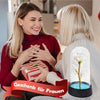 Une femme en haut rouge offre une rose en verre avec une lumière LED à une autre femme.