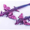A pair of 3D printed articulated dragon fidget figurines in iridescent pink and blue colors.
