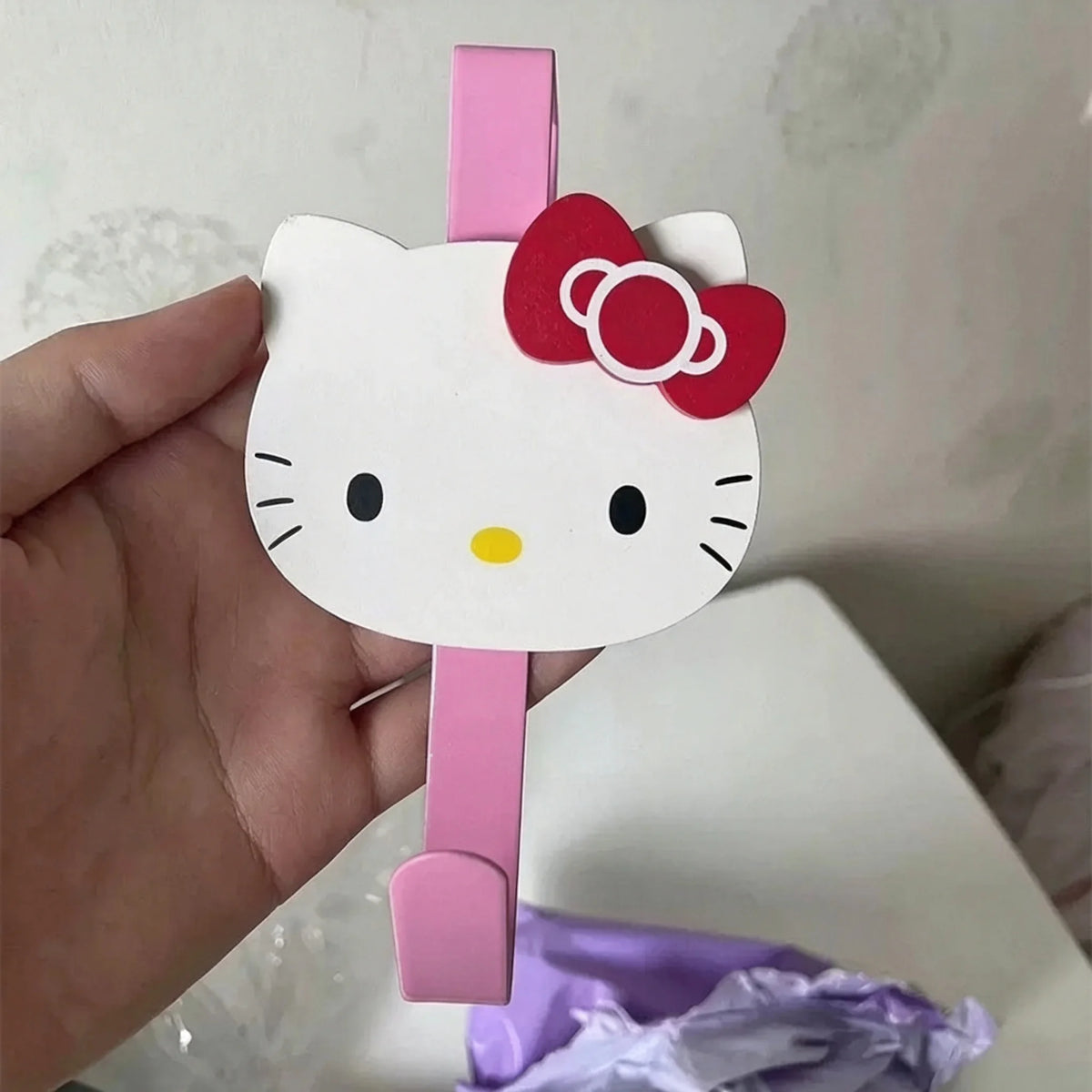 A hand holds a pink and white cartoon cat shaped over-the-door hook for storage.