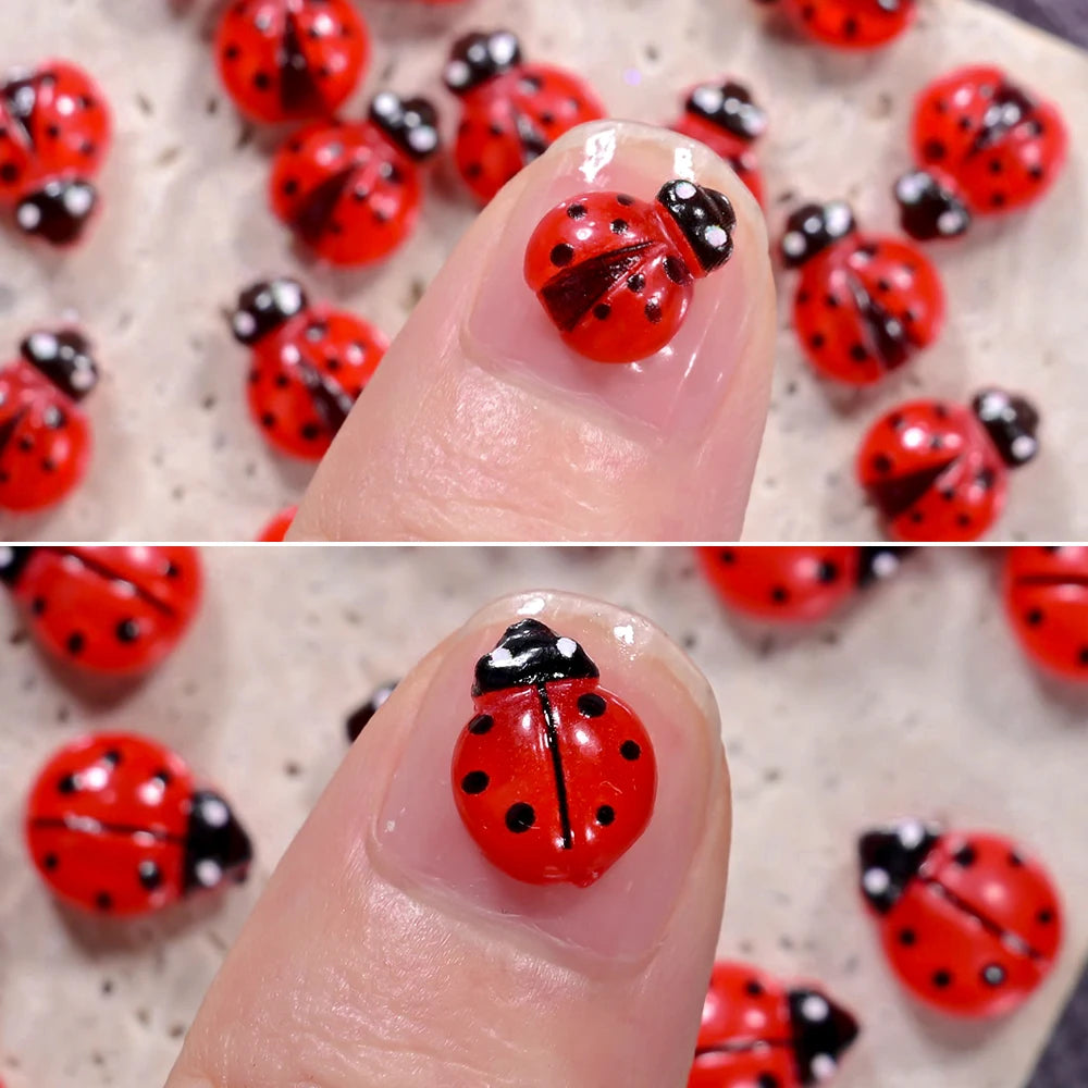 Close-up of a finger displaying red and black ladybug nail art charms on a white background.