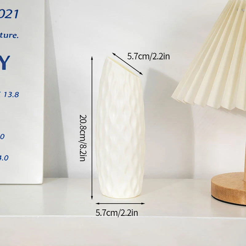 Eine weiße, strukturierte Plastikblumenvase auf einem weißen Regal neben einer Lampe.