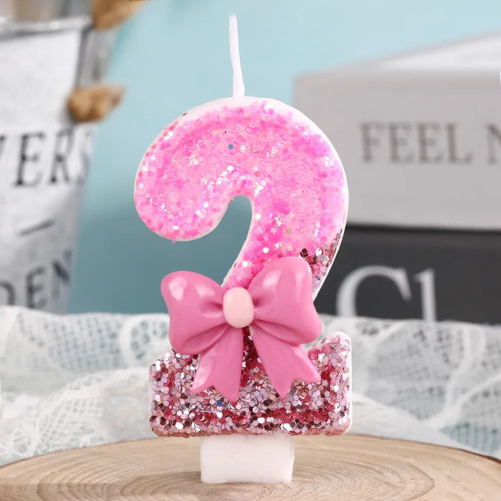 A pink glitter birthday candle shaped like the number 9 with a pink bow on a white base.