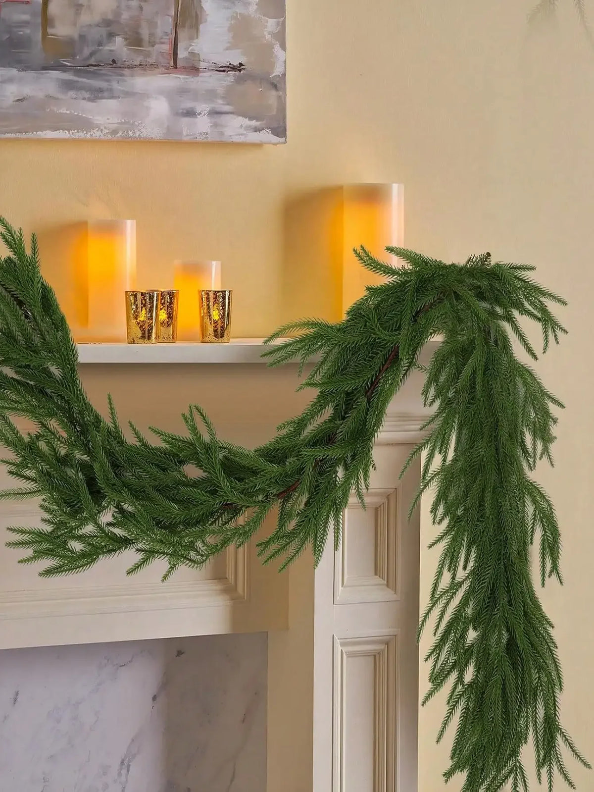 A long, lush green artificial Norfolk pine garland draped over a white mantelpiece with glowing candles.