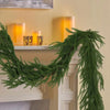 A long, lush green artificial Norfolk pine garland draped over a white mantelpiece with glowing candles.