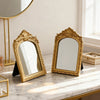 A pair of ornate gold-framed vanity mirrors with arched carvings resting on a marble surface.