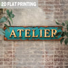 A vintage industrial metal wall sign with the word ATELIER in gold lettering mounted on a distressed turquoise metal plaque a