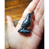 Handcrafted obsidian crow statue with etched lines held in a person's hand.