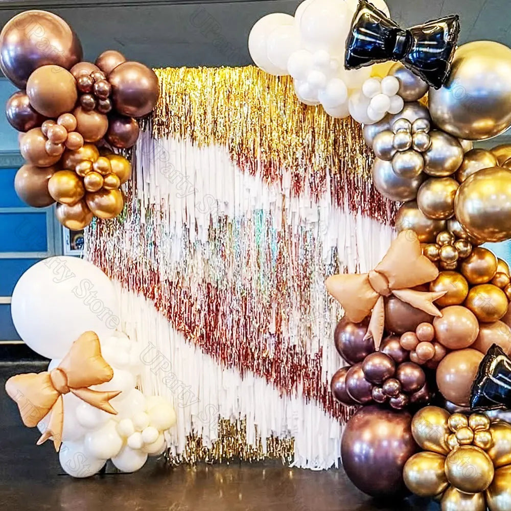 A party backdrop decorated with metallic gold and silver foil fringe curtains and round balloons.