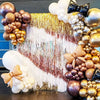 A party backdrop decorated with metallic gold and bronze balloons and fringe curtains.