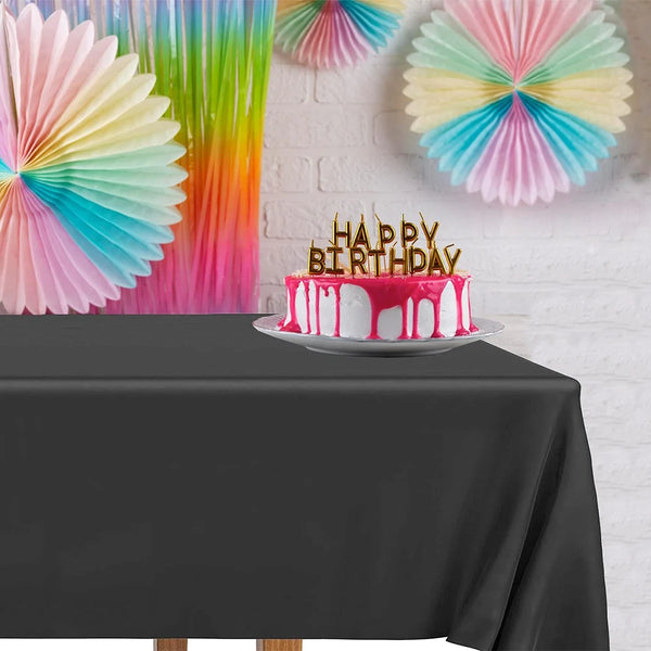 A pink and blue birthday cake with candles sits on a black tablecloth in front of a white brick wall.