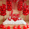 Eine Anordnung roter herzförmiger Ballons, die von einer Decke herabhängen und um ein Bett herum angeordnet sind.