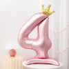 A pink foil balloon shaped like the number four with a gold crown on top.