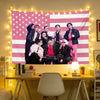 A group of five male Kpop idols posing in front of a pink and white American flag tapestry wall hanging decorated with string
