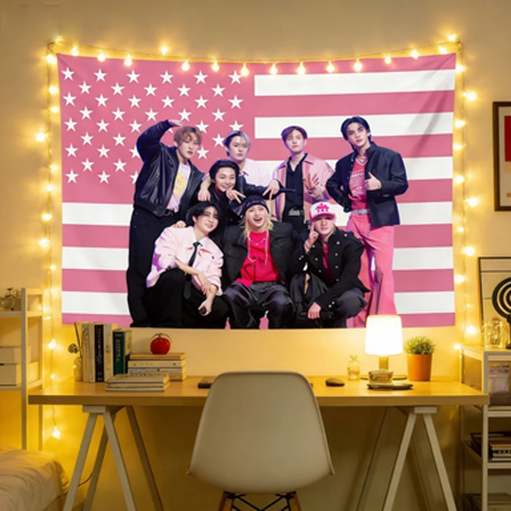 A group of five male Kpop idols posing in front of a pink and white American flag tapestry wall hanging decorated with string