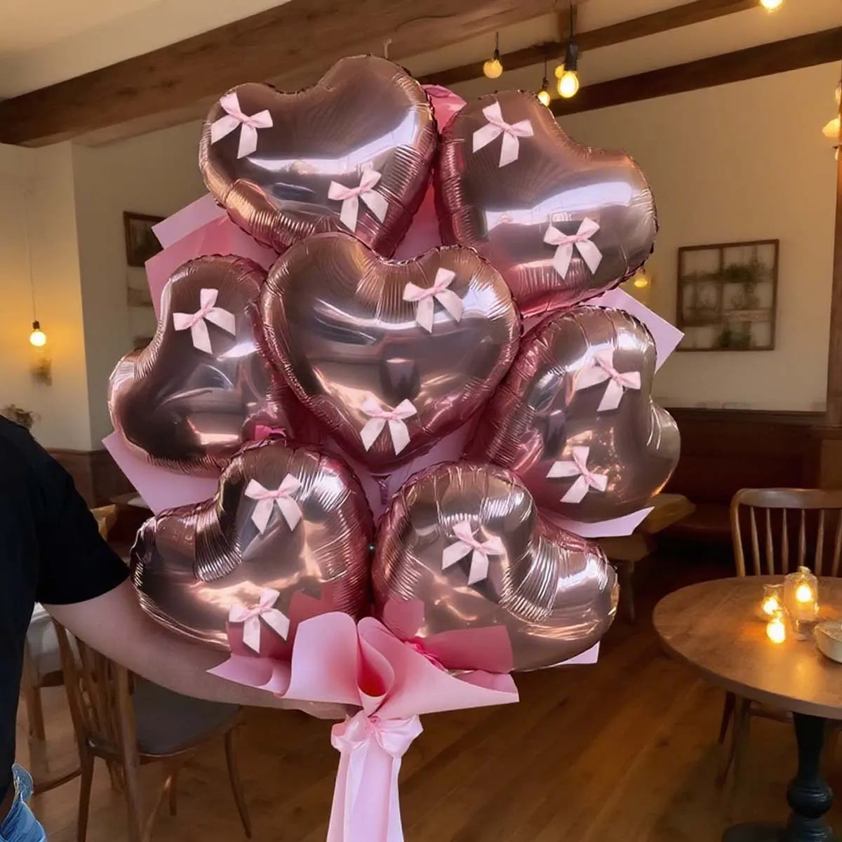 A bouquet of pink heart-shaped foil balloons tied with ribbons, held by a person.